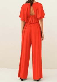 Jumpsuit rouge avec une coupe décontractée, des manches volant, un dos ouvert, une taille élastique et des jambes larges.