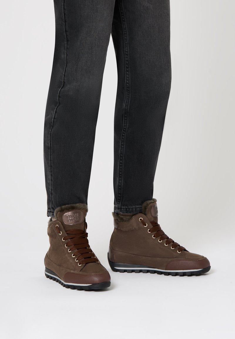 Stivaletti alti marroni in suede con fodera in pelliccia morbida, presentano lacci marroni, occhielli dorati e una suola in gomma texturizzata.