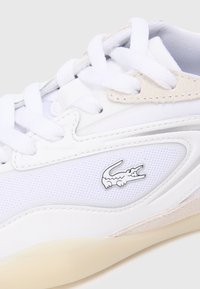 Baltas sporta apavi ar acs materiālu un ādu, ar sudraba Lacoste logo, apaļām auklām un krēmīgu gumijas zoli.