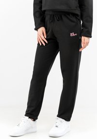 Black sweatpants with a drawstring waist, featuring a small pink logo on the thigh, side pockets, and a slim-fit design.