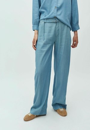 Lyseblå jeans med vidde i benene og en afslappet pasform. Har snøre i taljen, sidelommer og en glat tekstur. Kombineret med brunt fodtøj.