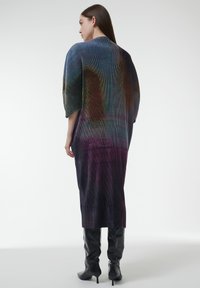 Lange, kleurrijke jurk met een geribbeld textuur en een verloop van kleuren van blauw naar paars, gedragen met elegante zwarte stiletto laarzen.