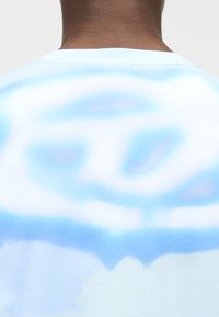 Πίσω μέρος του λαιμού και των ώμων ενός ατόμου που φοράει ένα ελαφρώς μπλε και άσπρο πουκάμισο με φωτεινό μοτίβο δέματος με θολό κυκλικό σχέδιο.