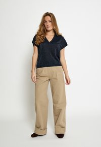 Top a maniche corte scollo a V color navy con simpatici riflessi metallici, abbinato a pantaloni kaki larghi a vita alta. Tessuto morbido e strutturato, orli risvoltati.