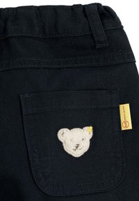 Schwarze Baumwollhose mit einer Gesäßtasche, die mit einer weißen Bärenkopf-Stickerei und einem kleinen gelben Akzent versehen ist. Anhänger mit Markenlogo befestigt.