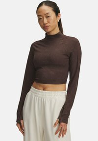Bruine cropped lange mouwen top met een hoge hals, gemaakt van gladde stof, met een aansluitend ontwerp en subtiele stikdetails. Witte broek met een elastische taille.