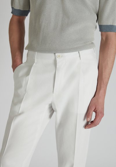 Polo de punto ligero en azul grisáceo con un diseño de malla texturizada, combinado con pantalones blancos de tiro alto que presentan plisados en la parte delantera y cierre de botón.