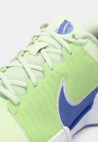 Αθλητικό παπούτσι σε ανοιχτό πράσινο χρώμα με δικτυωτό πάνω μέρος, υφασμάτινες λεπτομέρειες, μπλε λογότυπο Nike swoosh και αντίθεση λευκής σόλας. Οι κορδόνες είναι σε ανοιχτό πράσινο.