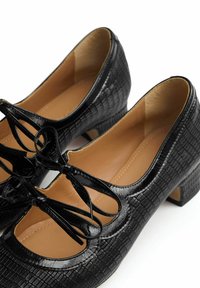 Czarne lakierowane buty na niskim obcasie z fakturą krokodyla i ozdobną kokardą z przodu, widziane z góry.