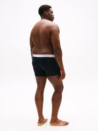 Boxer blu navy con elastico bianco sulla vita che presenta il logo "TOMMY HILFIGER". Il modello è in piedi di lato, mostrando la schiena nuda.