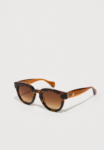 Lunettes de soleil en écaille de tortue avec des verres dégradés marron, forme géométrique en œil de chat, et branches accentuées en orange avec un détail en métal du logo.