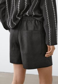 Black linen shorts with an elastic waistband and two back pockets. The fabric has a subtle texture, offering a relaxed fit and streamlined design.