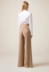 Pantalones de pierna ancha en color beige, hechos de una tela suave, con cintura alta, bolsillos traseros y un acabado limpio. Combinados con una camisa blanca ajustada.