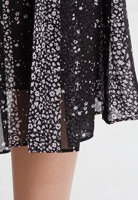 Tessuto nero con motivo floreale, caratterizzato da fiori grigio chiaro e bianchi. Presenta una texture leggera, un design fluido e un aspetto stratificato.