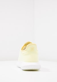 Gul nät sneakers med vadderad häl, vit sula och subtil branding på baksidan. Har en texturerad yta för andningsförmåga.