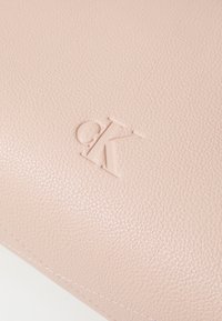 Clutch in pelle rosa chiaro con superficie testurizzata ed logo CK in rilievo. Dettaglio di cuciture evidente lungo il bordo.