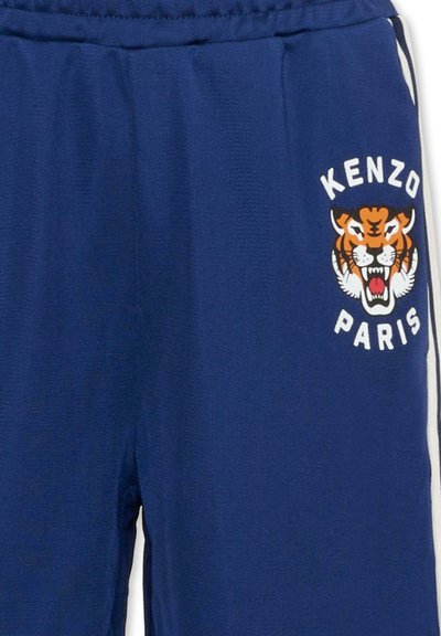 Niebieskie sportowe spodnie z teksturowanej tkaniny z białymi paskami po bokach. Na froncie grafika tygrysa oraz białe napisy "KENZO PARIS".