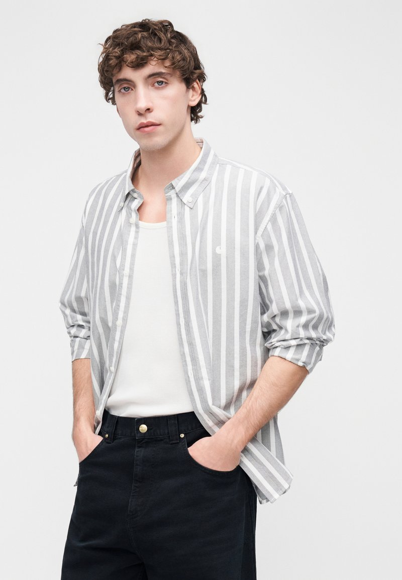 Skjorte med knapper i lys grå med hvide lodrette striber, kombineret med en hvid tanktop og mørke bukser. Glat stof, afslappet pasform.