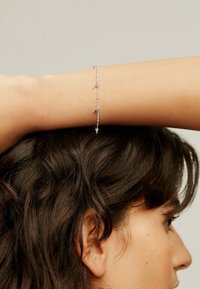 Pulsera de plata con pequeños charms en forma de estrella y luna creciente. Diseño de cadena delicada, que presenta una mezcla de elementos lisos y texturizados.