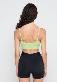 Zielony prążkowany biustonosz typu bralette z regulowanymi ramiączkami; w komplecie z czarnymi dopasowanymi szortami. Prosty design, gładka faktura i naturalny wygląd tkaniny.