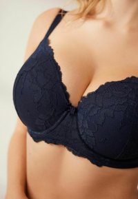 Senkrechtblaue Spitzen-BH mit Blumenmuster und Netzdetails. Verfügt über gepolsterte Cups und verstellbare Träger. Dekorativer Bogen in der Mitte.