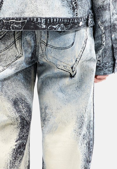 Conjunto de chaqueta y pantalones de denim con un estampado gráfico en azul claro y negro, con bolsillos visibles y detalles de costura en contraste.
