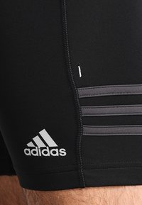 Pantalones cortos deportivos negros con una textura suave, que presentan tres rayas grises en el costado y un logo blanco de Adidas cerca del dobladillo.