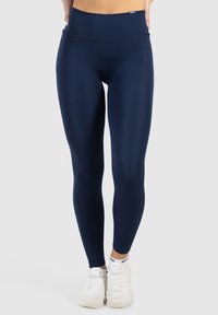 Marinblå leggings med ett mjukt, elastiskt tyg, hög midja och sidofickor, i kombination med vita träningssneakers.