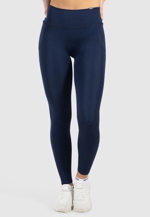 Navyblauwe legging van een gladde, rekbare stof, met een hoge tailleband en zijzakken, gecombineerd met witte sportschoenen.