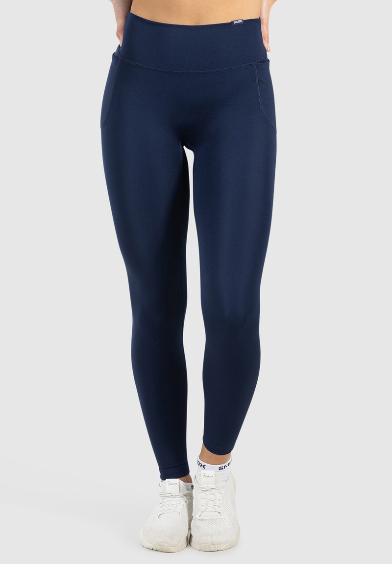 Marinblå leggings med ett mjukt, elastiskt tyg, hög midja och sidofickor, i kombination med vita träningssneakers.