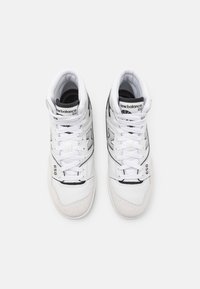 High-top sneakers with white leather and black accents. Features perforated toe box, laces, padded collar, and logo on tongue. Model 650.