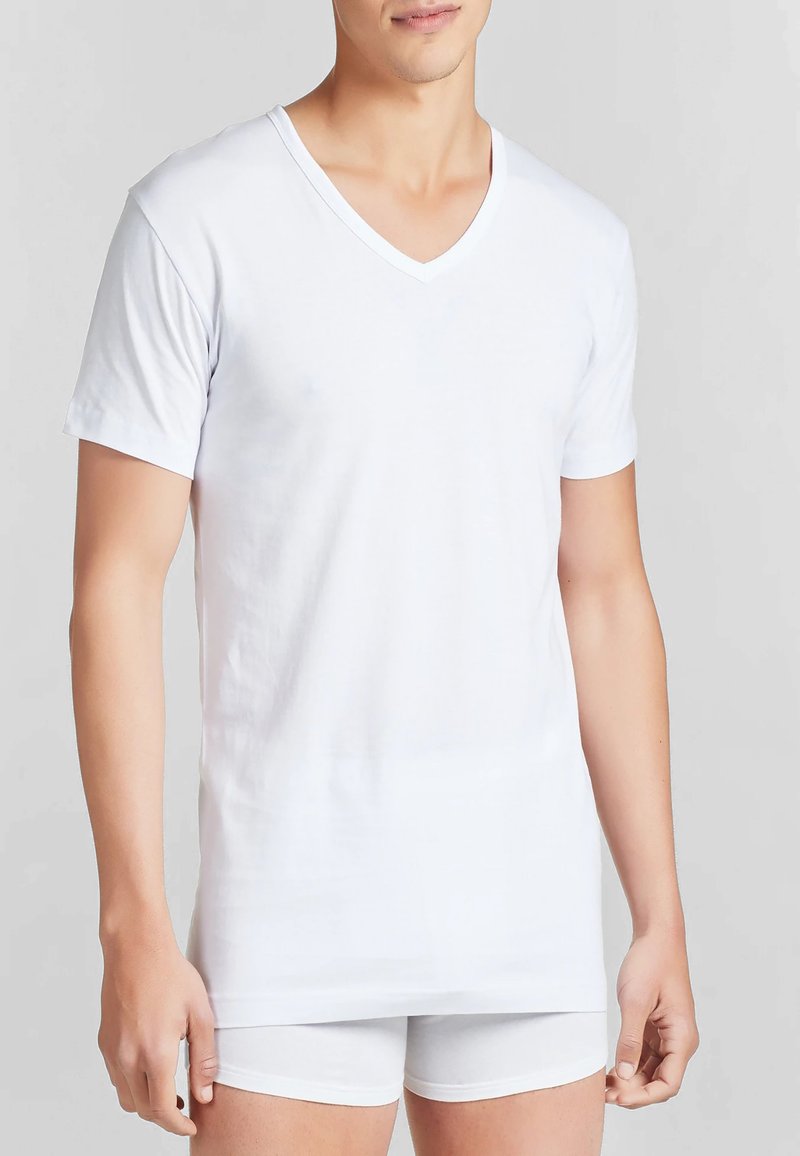 T-shirt bianco a maniche corte con scollo a V realizzato in tessuto leggero, caratterizzato da un design semplice e una texture liscia, abbinato a pantaloni corti bianchi.
