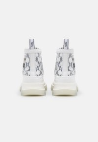 Sneakers alta con superiore trasparente e motivo a zigzag grigio, accenti bianchi e una suola spessa e cremosa. La vista posteriore mostra il marchio.