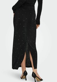 Falda negra ajustada con adornos blancos visibles, aberturas laterales y una tela de textura suave. Combinada con zapatos de tacón negro.