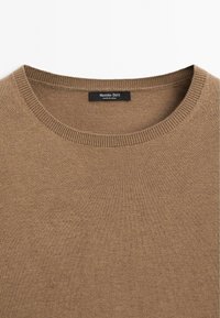 Brązowy dzianinowy sweter z okrągłym dekoltem. Tekstura jest gładka z subtelnymi szwami. Metka informuje "Massimo Dutti, wyprodukowano w Chinach."