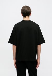 Czarny bawełniany t-shirt o luźnym kroju, z krótkimi rękawami i okrągłym dekoltem. Gładka faktura bez widocznych wzorów czy grafik.