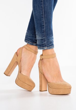 Sandales à talons en daim beige avec une semelle compensée et une bride de cheville à boucle, présentées avec un jean en gros plan.