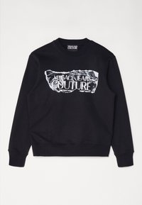 Svart sweatshirt med ett skrynkligt vitt tryck med texten "VERSACE JEANS COUTURE" över framsidan. Ribbstickade muddar och fåll.