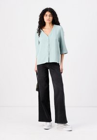 Blusa blu chiaro con scollo a V e maniche a tre quarti, abbinata a jeans neri a vita alta ampi e sneaker bianche con plateau.