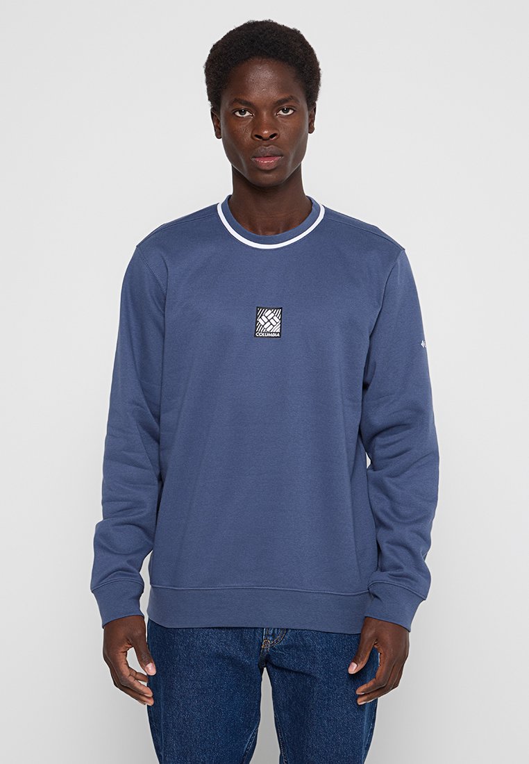 Felpa blu navy con scollatura rotonda, dettagli sui polsini bianchi e una toppa logo in bianco e nero sul petto. Tessuto morbido, maniche lunghe.