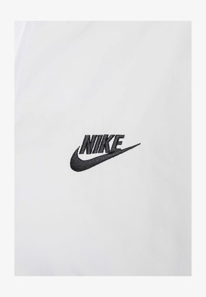 White fabric windbreaker featuring a small black embroidered Nike logo on the left side, smooth texture, and simple design.