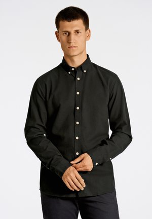 Musta napitettava paita, jossa on terävä kaulus, pienet beige napit, pitkät hihat ja sileä pinta. Rentoa istuvuutta.