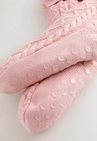 Calzini rosa lavorati a maglia con un design a intreccio e motivi a puntini rialzati sulle suole per una maggiore consistenza e presa.