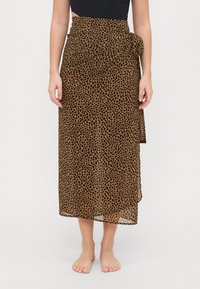 Jupe longue en voile marron à pois noirs, nouée à la taille, au design fluide, arrivant aux chevilles. Tissu léger et texturé.