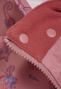 Vattentåligt rosa tyg med en plyschfleecefoder i korall. Har två plastknappar och ett dekorativt marinmönster inuti.