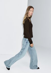 Brown fitted knit sweater paired with light blue wide-leg jeans. The outfit features a simple design and is complemented by black shoes.
