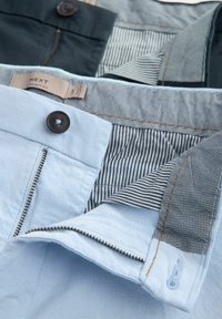 Helleblaue und dunkelgrüne Hosen mit Knopfverschlüssen, Reißverschluss und gestreiftem Futter. Auffällige kontrastierende Nähte und strukturierter Stoff.