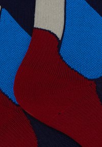 Calzini lavorati a maglia colorati con motivi geometrici blu, rossi, navy e beige, polsino a coste e texture morbida.