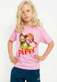 Rosa Baumwoll-T-Shirt mit einem grafischen Druck eines Mädchens mit orangenen Zöpfen. Fetter "PIPPI"-Text in Rot. Rundhalsausschnitt und kurze Ärmel.