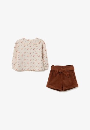 Beige Langarmoberteil mit floralem Muster und gewelltem Kragen, kombiniert mit braunen Cordshorts mit einer Schleife am Taillenbund.
